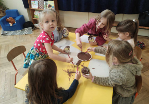 Zdjęcie przedstawia dzieci malujące brązową farbą papierowe kule.