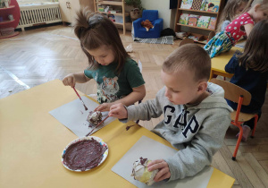 Zdjęcie przedstawia chłopców malujących brązową farbą papierowe kule.