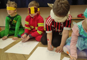 Na zdjęciu widzimy grupkę dzieci, które z zamkniętymi oczami rysują bałwana na kartonie.