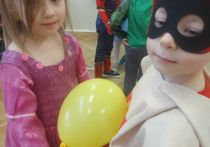 Na zdjęciu widzimy dziewczynkę i chłopca, którzy uczestniczą w zabawie. Pomiędzy swoimi brzuchami trzymają żółtego balona.