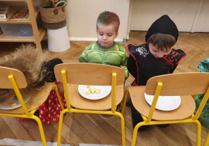 Na zdjęciu widzimy trójkę dzieci, które uczestniczą w zabawie. Mają za zadanie zjeść kawałki jabłka położone na talerzyku bez użycia rąk.