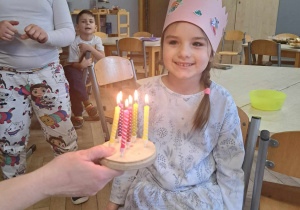 Zdjęcie przedstawia dziewczynkę przy torcie z zapalonymi świeczkami.