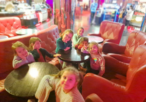 Zdjęcie przedstawia dziewczynki siedzące na fotelach w holu kina.