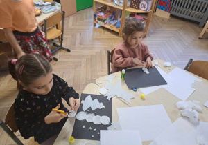 Zdjęcie przedstawia dziewczynki klejące i wycinające elementy do pracy plastycznej.