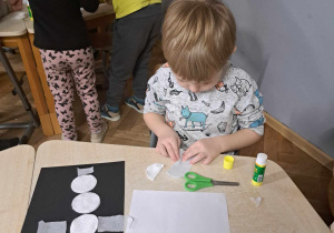 Zdjęcie przedstawia chłopca tworzącego swoją pracę z użyciem płatków kosmetycznych.