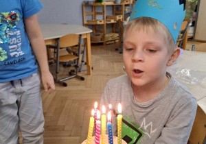 Zdjęcie przedstawia chłopca przy świeczkach z zapalonymi świeczkami.