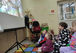 Zdjęcie przedstawia dzieci siedzące przed rzutnikiem. Dzieci patrzą na wyświetlany obraz.