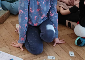 Zdjęcie przedstawia dziewczynkę przyglądającą się rozrzuconym na podłodze karteczkom z sylabami.