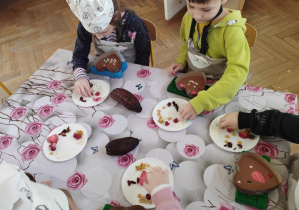 Na zdjęciu widzimy dzieci, które tworzą własną dekorację na czekoladzie.