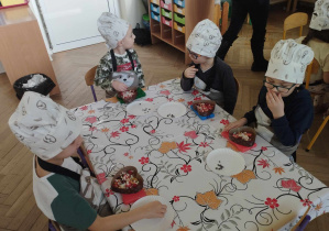 Na zdjęciu widzimy grupkę dzieci, które tworzą własne dekoracje na czekoladzie oraz degustują czekoladę.