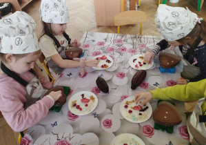 Na zdjęciu widzimy grupkę dzieci, które tworzą własne dekoracje na czekoladzie.