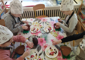 Na zdjęciu widzimy grupkę dzieci, które tworzą własne dekoracje na czekoladzie.
