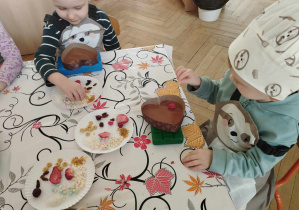 Na zdjęciu widzimy dwójkę chłopców, którzy układają na czekoladzie produkty.