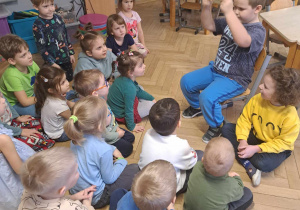 Zdjęcie przedstawia chłopca pokazującego ilustracje w książce innym dzieciom.