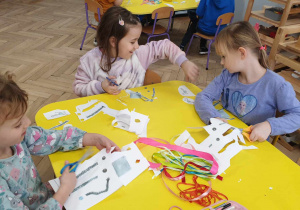 Zdjęcie przedstawia trzy dziewczynki wycinające nożyczkami elementy do wykonanania pracy plastycznej.
