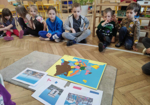 Zdjęcie przedstawia dzieci siedzące wokół pomocy dydaktycznych - mapy Europy oraz zdjęć związanych z Francją.