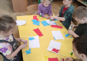 Zdjęcie przedstawia dzieci siedzące przy stole. Dzieci wykonują flagę Francji metodą wydzieranki.