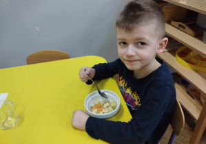 Zdjęcie przedstawia chłopca siedzącego przy stoliku, uśmiechjącego się do zdjęcia.