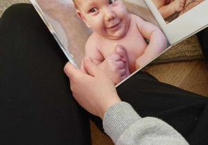 Zdjęcie przedstawia dziecko oglądające fotografie przedstawiające niemowlaka.