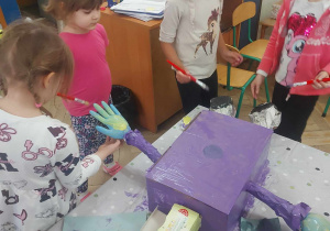 Zdjęcie przedstawia dzieci malujące farbą część robota
