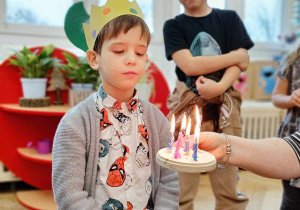 Chłopiec zdmuchuje świeczki na symbolicznym torcie.