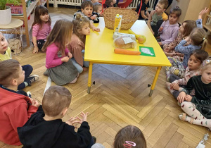 Dzieci siedzą dookoła stołu, na którym zgromadzone są różne produkty spożywcze.