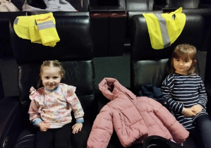 Na zdjęciu widzimy dwie dziewczynki, które siedzą w sali kinowej i oczekują na film.