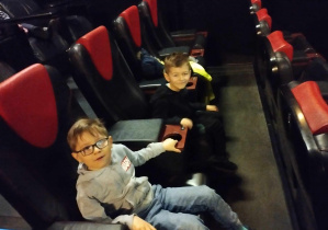 Na zdjęciu widzimy dwóch chłopców, którzy siedząc na fotelach oczekują filmu "Ekipa z Dżungli".
