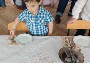 Dzieci szykują stół , ustawiają talerzyki, widelce itp