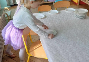 Dzieci szykują stół , ustawiają talerzyki, widelce itp