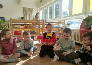 Zdjęcie przedstawia dzieci siedzące na podłodze. Jedno z nich trzyma papierowe czerwone serce.
