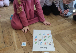 Zdjęcie przedstawia dziewczynkę układającą sudoku z kolorowymi skarpetkami. Reszta dzieci przygląda się czynności.