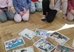 Zdjęcie przedstawia dzieci przyglądające się fotografiom położonym na podłodze. Fotografie przedstawiają różne dzieci.