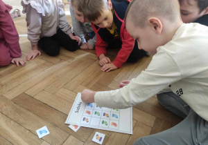 Zdjęcie przedstawia chłopca układającego sudoku z kolorowymi skarpetkami. Reszta dzieci przygląda się czynności.