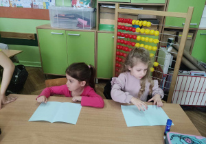 Zdjęcie przedstawia dwie dziewczynki siedzące w szkolnej ławce.
