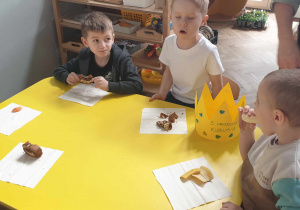 Zdjęcie przedstawia dzieci siedzące przy stoliku, jedząc ciasto i owoce.