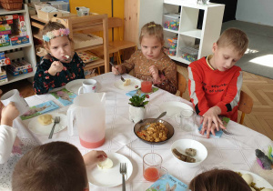Na zdjęciu widzimy grupkę dzieci, które jedzą wielkanocny obiad.