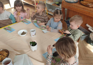 Na zdjęciu widzimy grupkę dzieci, które jedzą ciasta przyniesione przez rodziców.