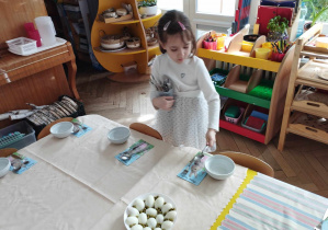 Na zdjęciu widzimy dziewczynkę, która rozkłada łyżki dla każdego dziecka.