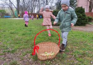 Zdjęcie przedstawia dzieci wrzucające do koszyka czekoladowe jajeczka.