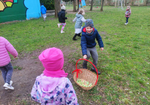 Zdjęcie przedstawia dzieci zbierające czekoladowe jajka do kosza.