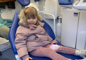 Zdjęcie przedstawia dziewczynkę siedzącą na fotelu dentystycznym.