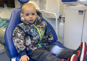 Zdjęcie przedstawia chłopca siedzącego na fotelu dentystycznym.