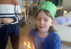 Zdjęcie przedstawia dziewczynkę dmuchającą świeczki na torcie.