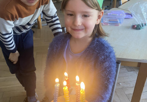Zdjęcie przedstawia dziewczynkę przy torcie urodzinowym z zapalonymi świeczkami.