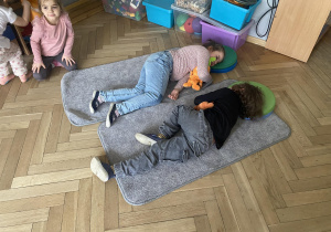 Zdjęcie przedstawia dwójkę dzieci leżącą na dywanikach.