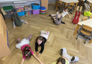 Zdjęcie przedstawia dzieci leżące na brzuchu na podłodze.