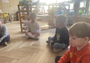 Zdjęcie przedstawia dzieci siedzące na podłodze z zamkniętymi oczami.