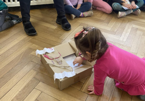 Zdjęcie przedstawia dziewczynkę wyjmującą kartkę z pudełka.