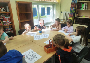 Zdjęcie przedstawia dzieci siedzące przy stole. Dzieci kolorują kwiaty.